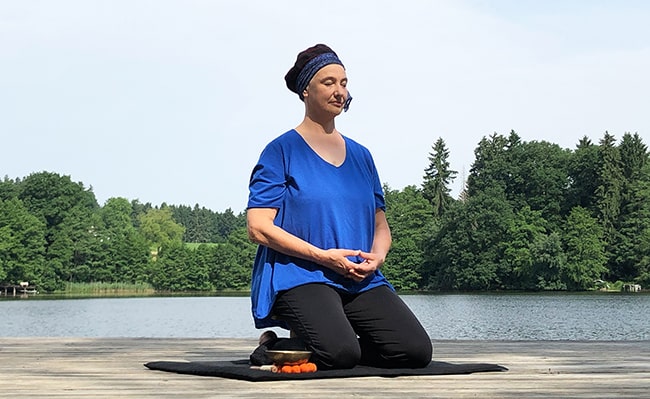 meditierende Frau auf einem Steg am See
